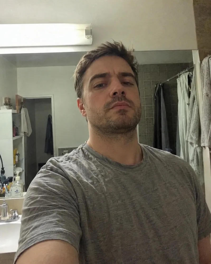 Antes de Foto Glow-Up: selfie de un chico con luz fluorescente en el baño, poco favorecedor para apps de citas
